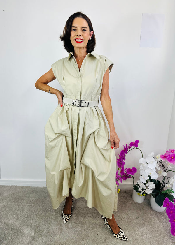 Woman wearing a light green dress with a belt, standing indoors with flowers in the background.