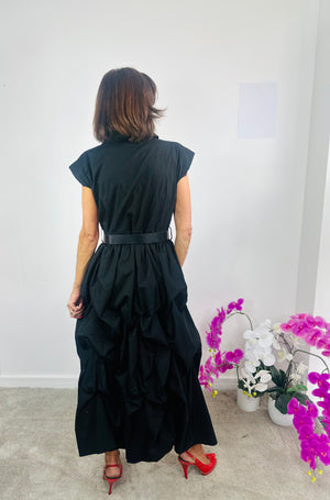Woman wearing a black dress with a white wall and decorative plants in the background