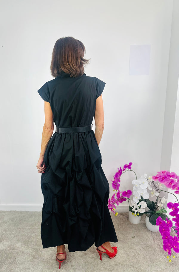 Woman wearing a black dress with a white wall and decorative plants in the background