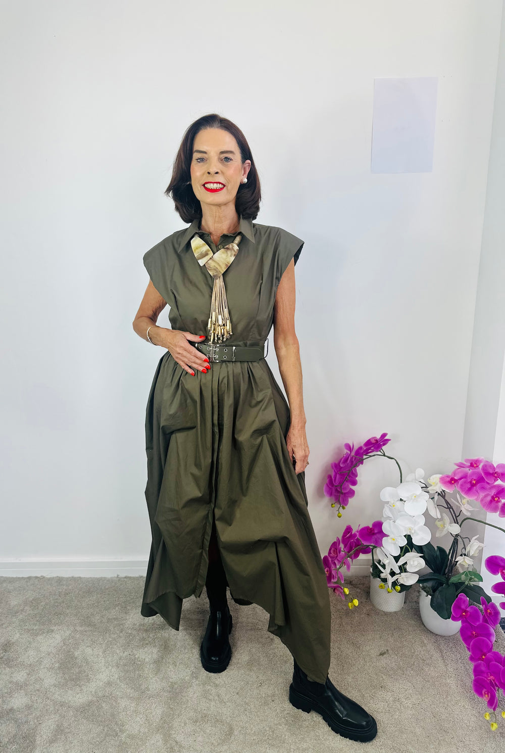 Woman in a green dress standing indoors with decorative plants in the background