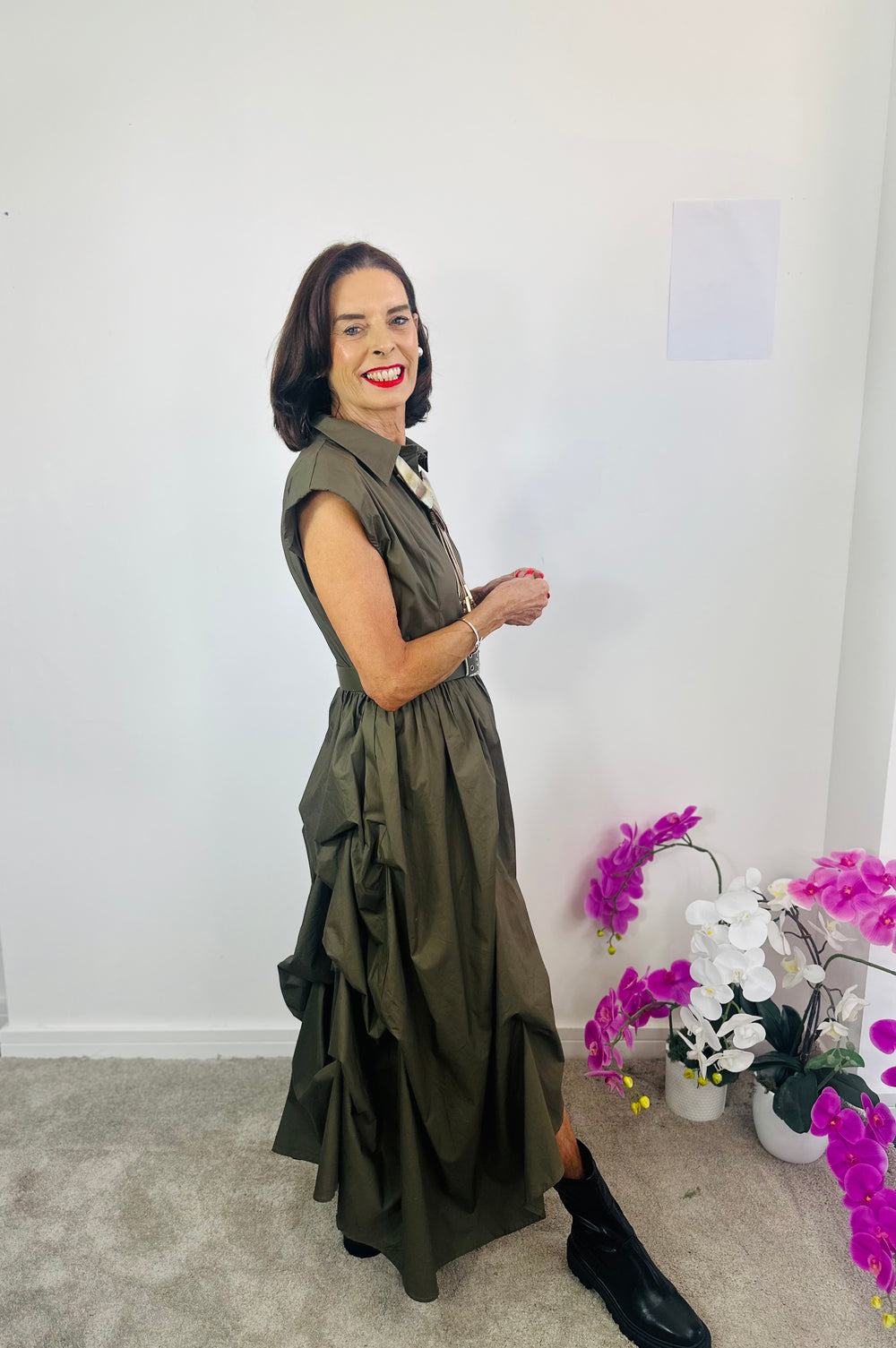 Woman in a green dress standing indoors with decorative plants in the background